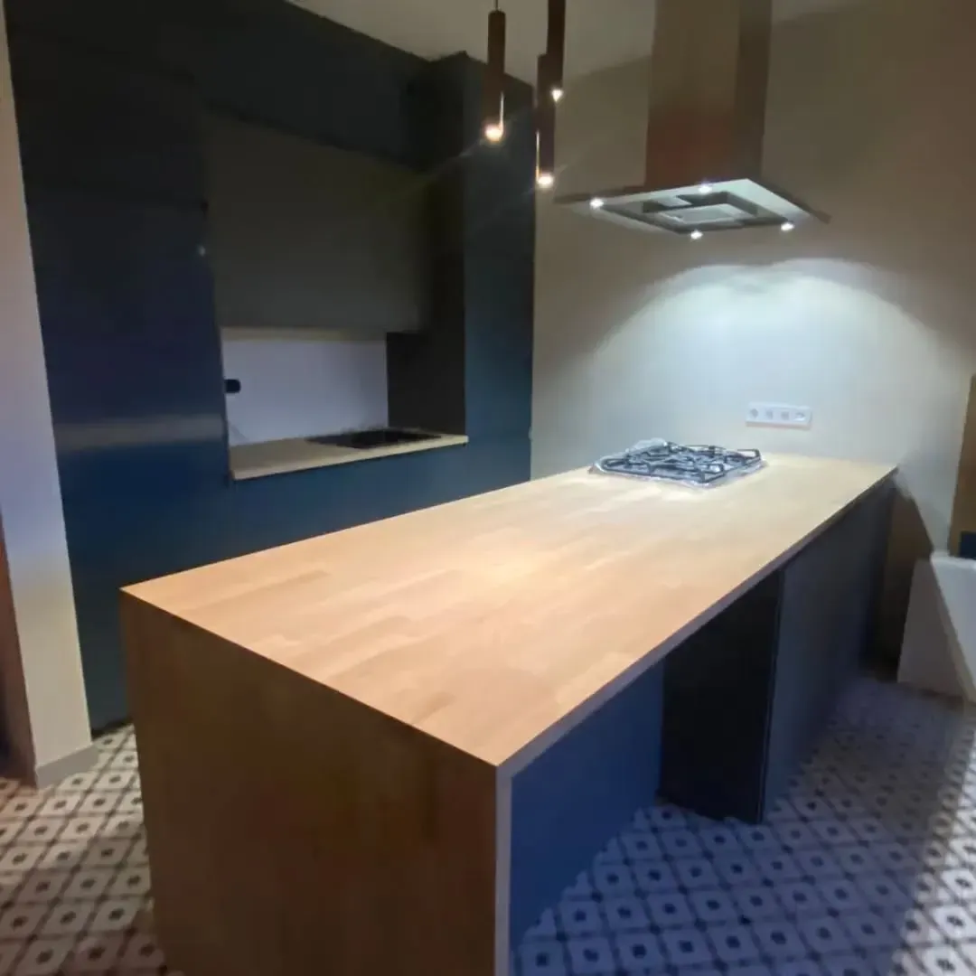 Cocina con gabinetes azules, isla de madera clara e iluminación cenital.