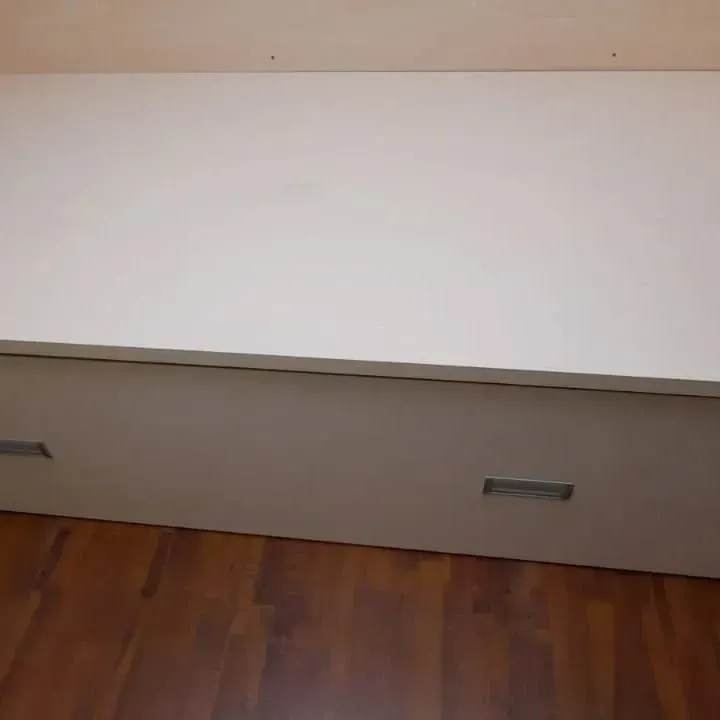 Mueble blanco con dos tiradores rectangulares sobre suelo de madera.