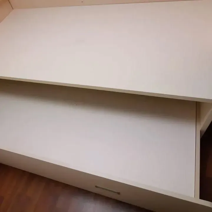 Estructura de cama blanca con cajón abierto, suelo de madera visible.
