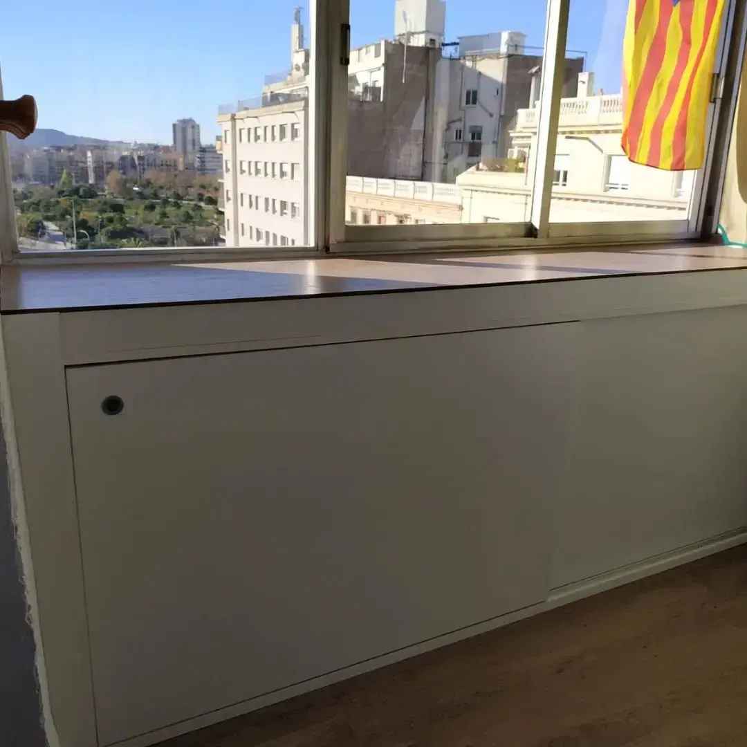 Armario blanco bajo una ventana con vistas a la ciudad. Una bandera cuelga a la derecha.