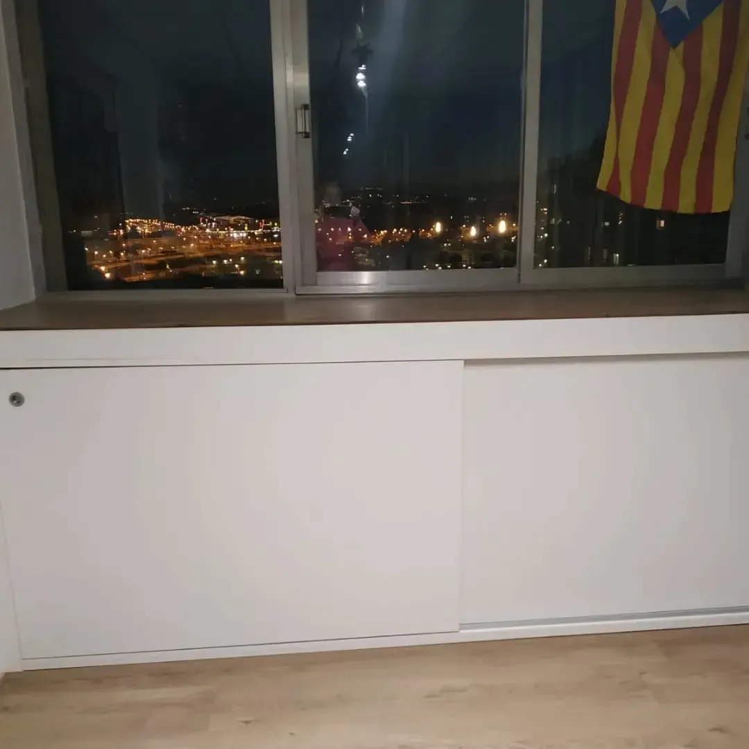 Armarios blancos debajo de una ventana con vistas a las luces de la ciudad, bandera catalana colgando.
