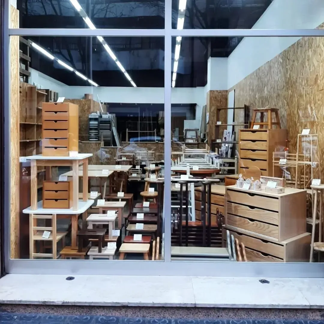 Escaparate de tienda de muebles de madera: mesas, taburetes, cajoneras, varios tamaños.