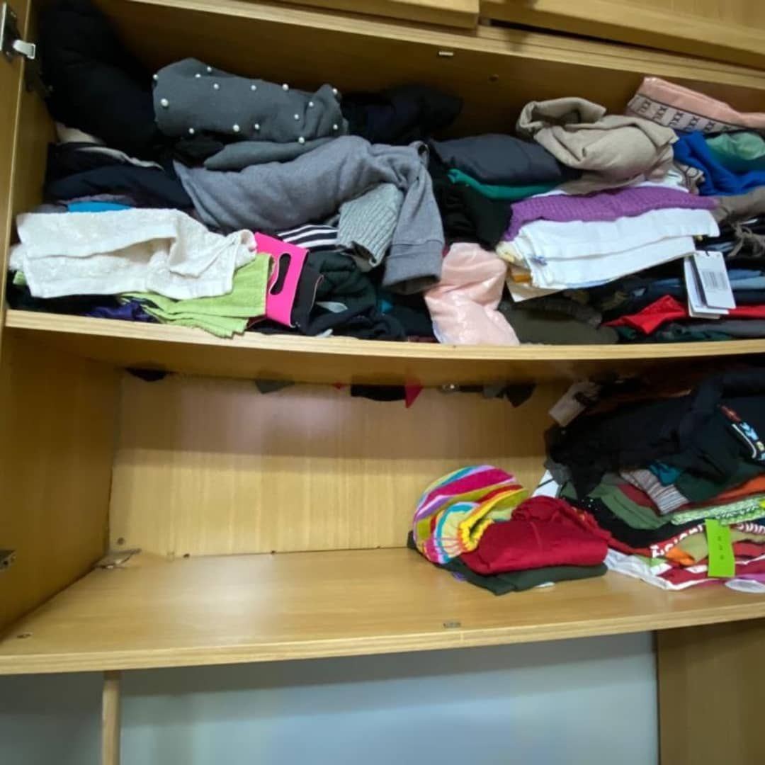 Armario de madera abierto lleno de ropa doblada en estantes.