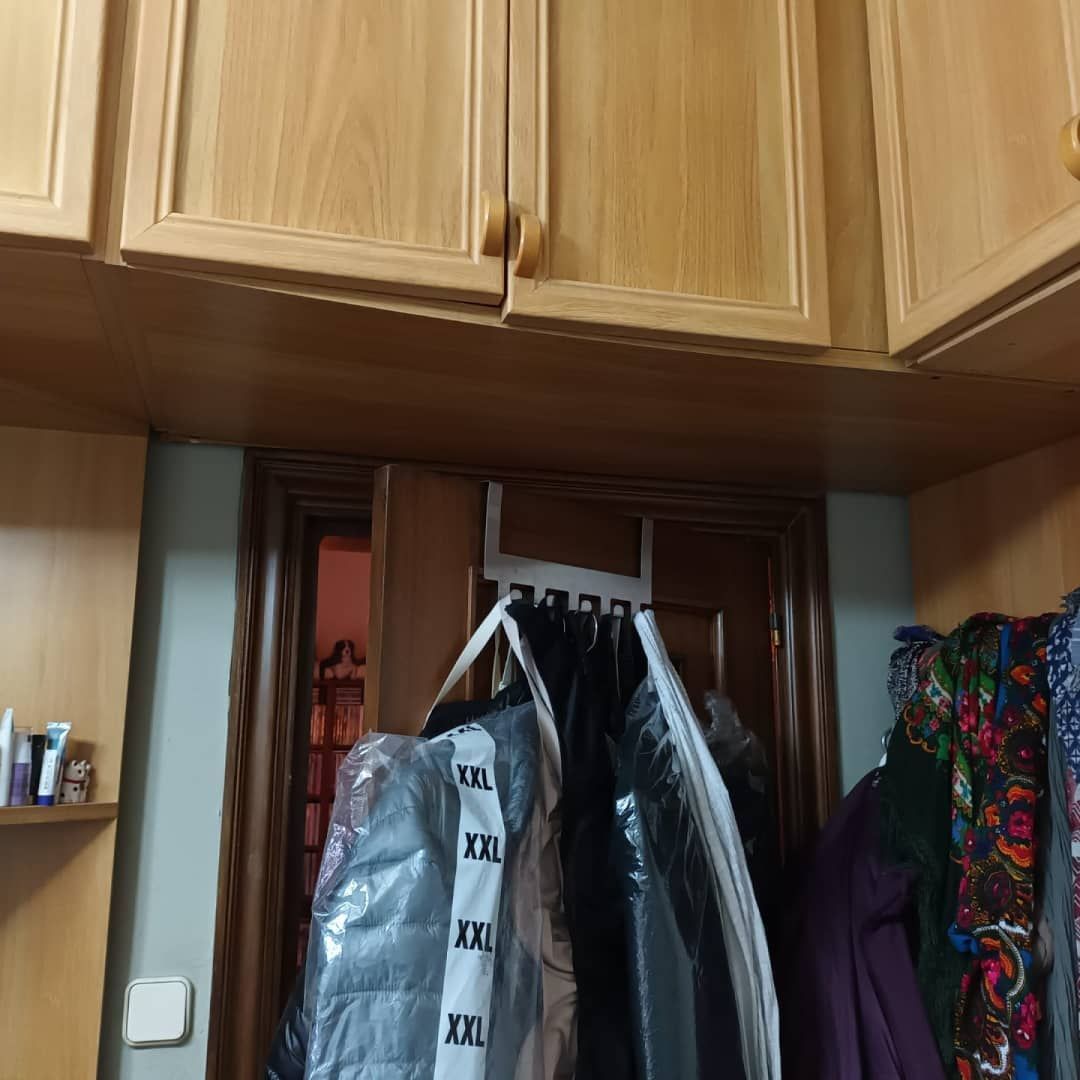 Armarios de madera sobre una puerta con ropa colgada, una bolsa de plástico transparente para ropa y estantes.