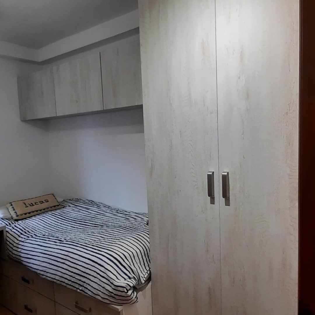 Dormitorio con una cama, ropa de cama a rayas, espacio de almacenamiento superior y un armario alto.