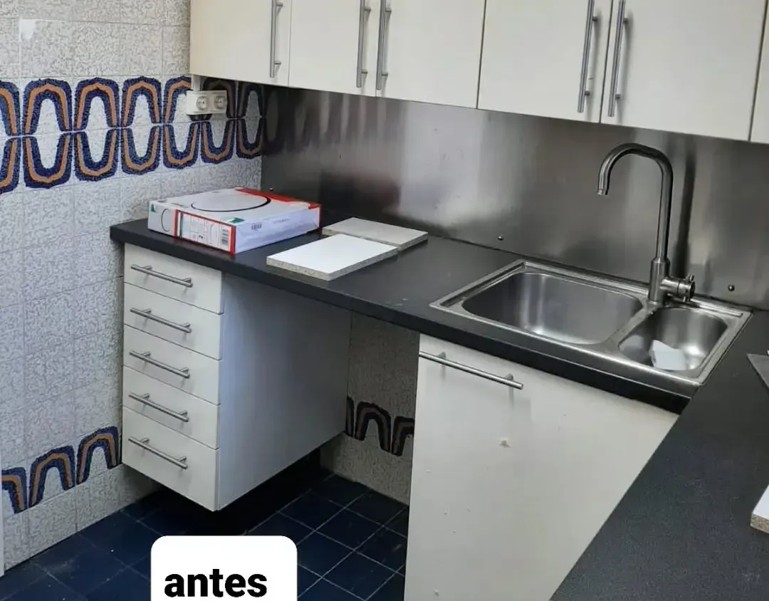 Encimera de cocina con salpicadero y fregadero de acero inoxidable; gabinetes blancos, paredes revestidas de azulejos.