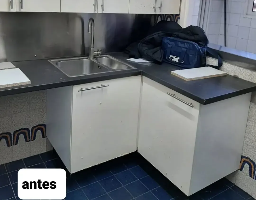 Rincón de cocina con fregadero, gabinetes blancos y encimera oscura; piso de baldosas azules con etiqueta 