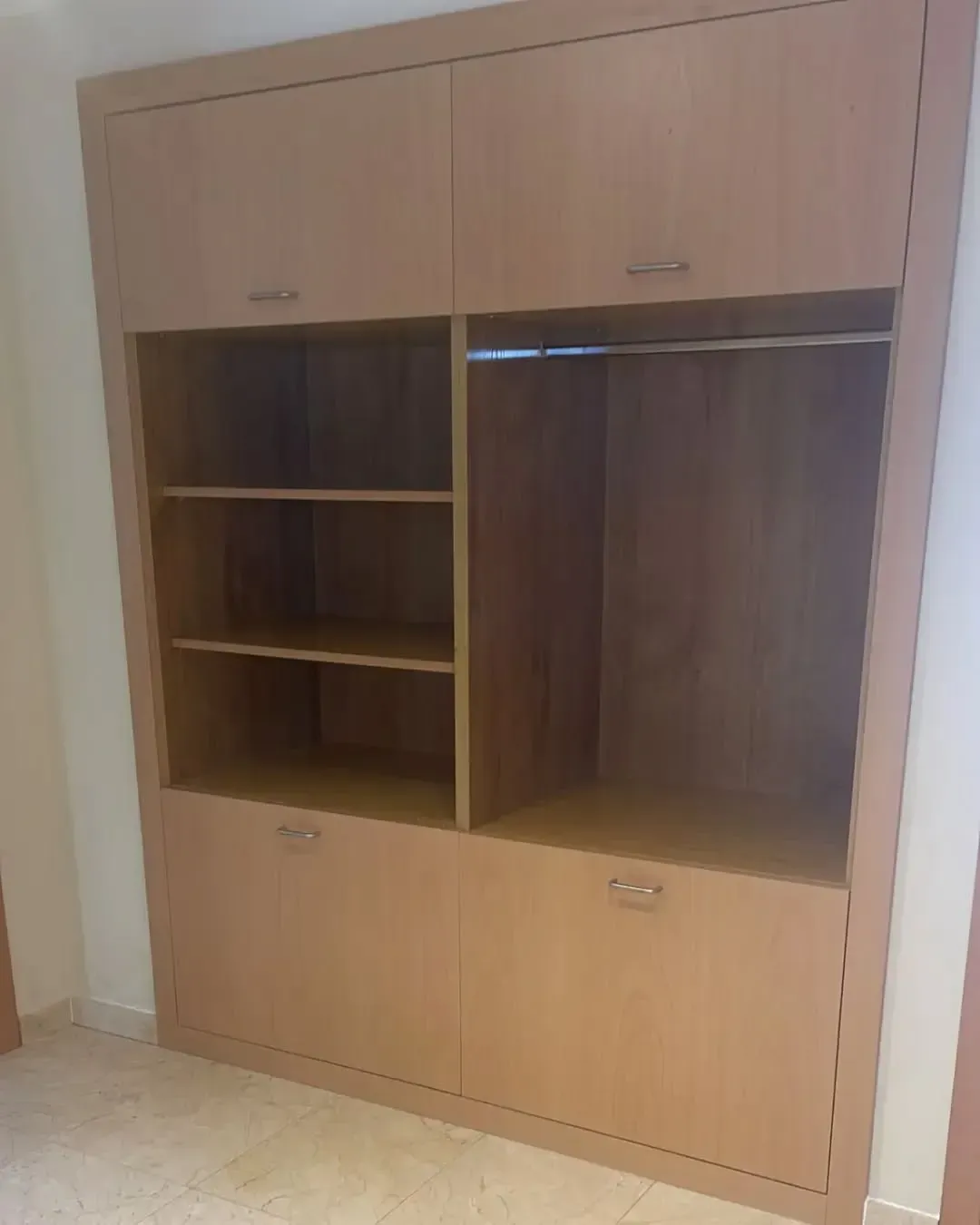 Armario de madera con estantes, barra para colgar y puertas de armario. Color marrón claro en una habitación vacía.