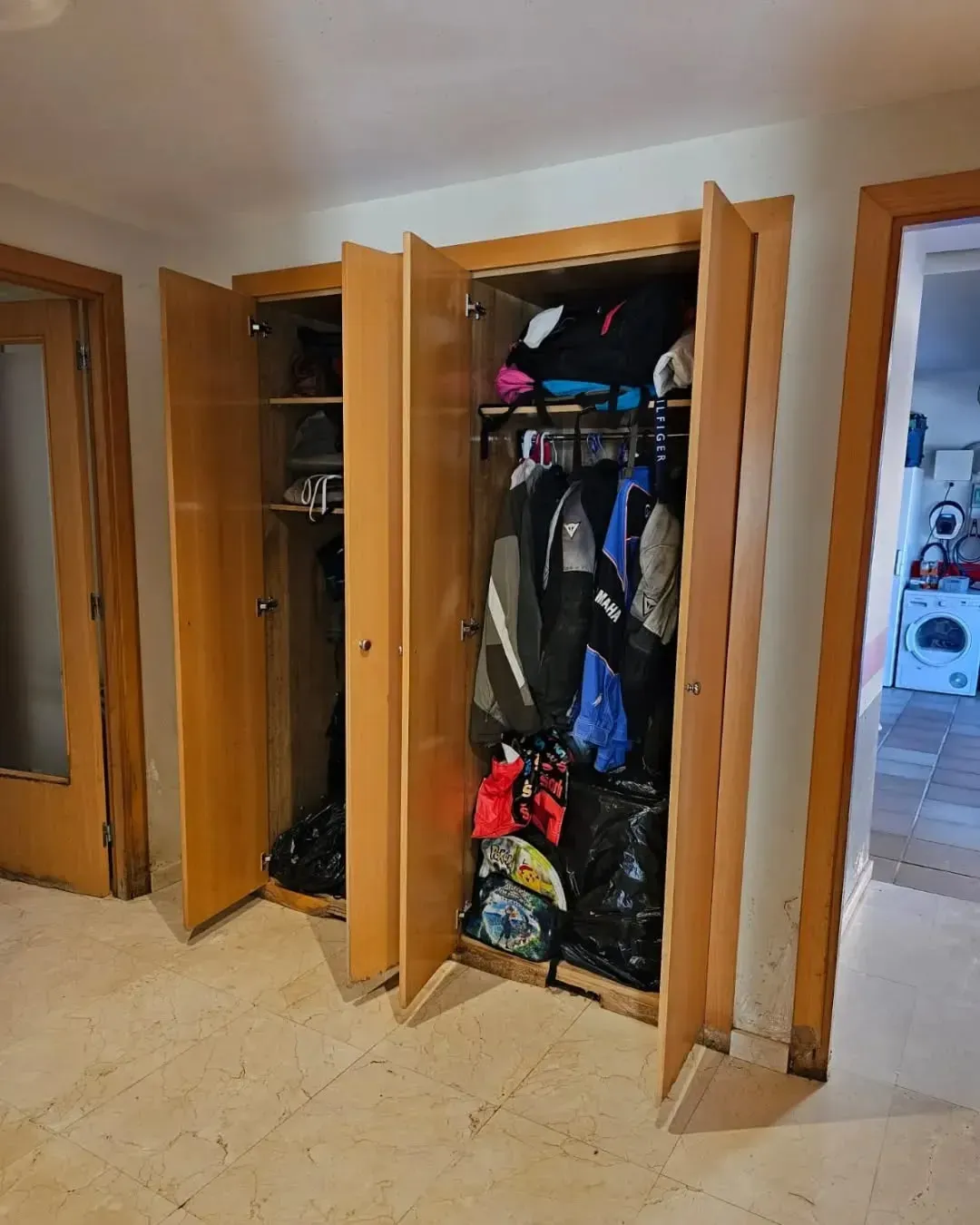 Armario con puertas plegables, lleno de abrigos, zapatos y bolsos en un pasillo.