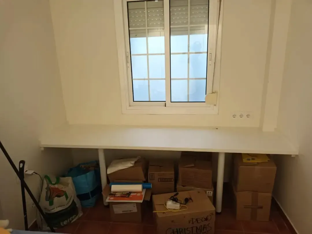 Una ventana con un escritorio largo debajo. Cajas de cartón y bolsas se guardan debajo del escritorio.