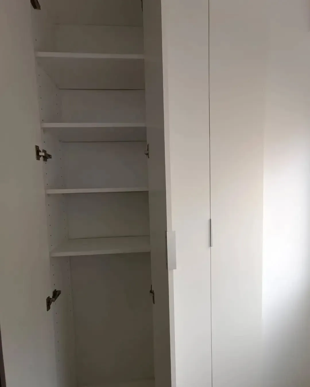 Interior de armario blanco con múltiples estantes; una puerta abierta.