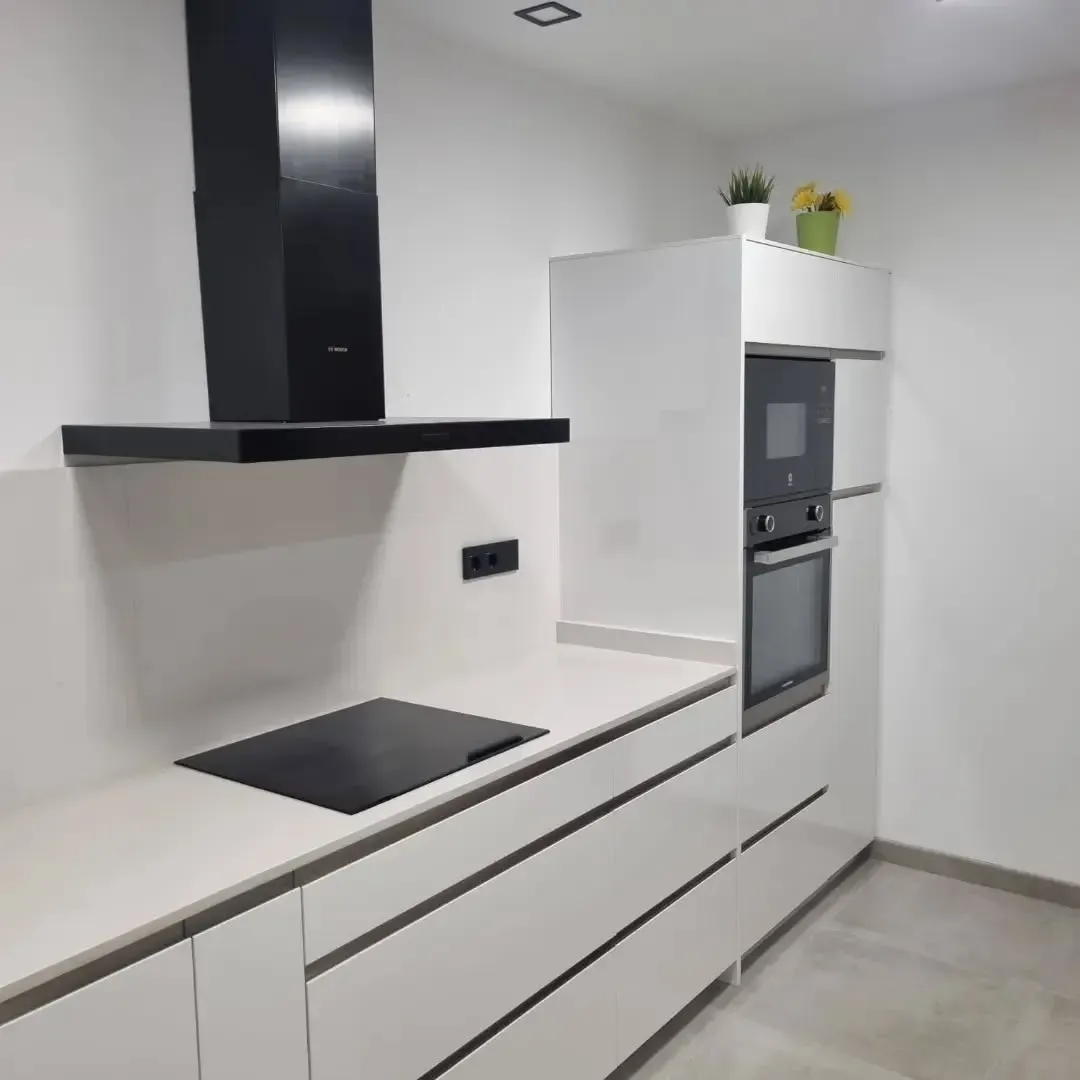 Cocina moderna blanca con electrodomésticos negros. Incluye horno, microondas y campana extractora.