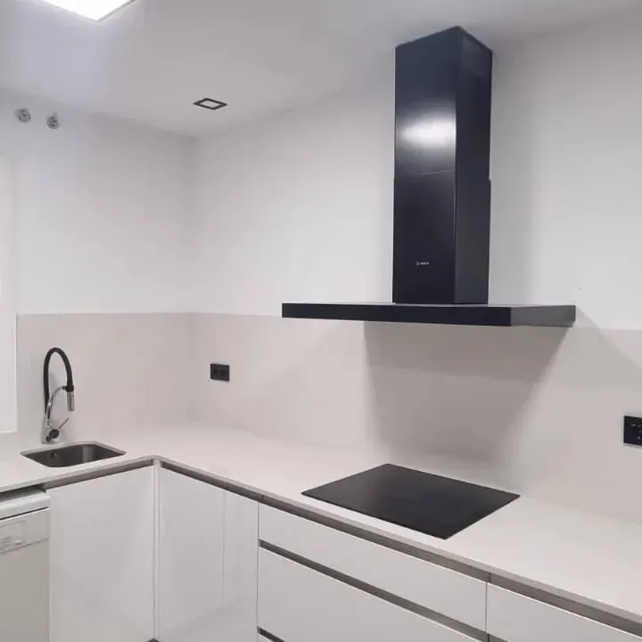 Cocina blanca moderna con campana extractora y anafe de color negro, fregadero y grifo de acero inoxidable.