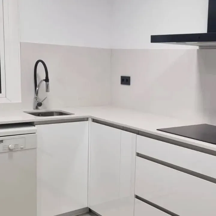 Cocina blanca moderna con fregadero de acero inoxidable, grifo negro y electrodomésticos empotrados.