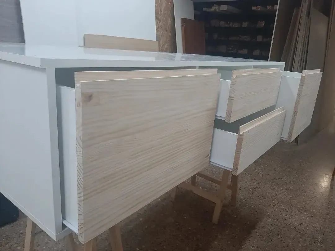 Mueble blanco con frentes de cajones de madera sin terminar; entorno de tienda.