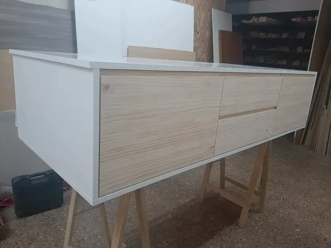 Mueble en tono blanco y madera con cajón sobre caballetes en taller.
