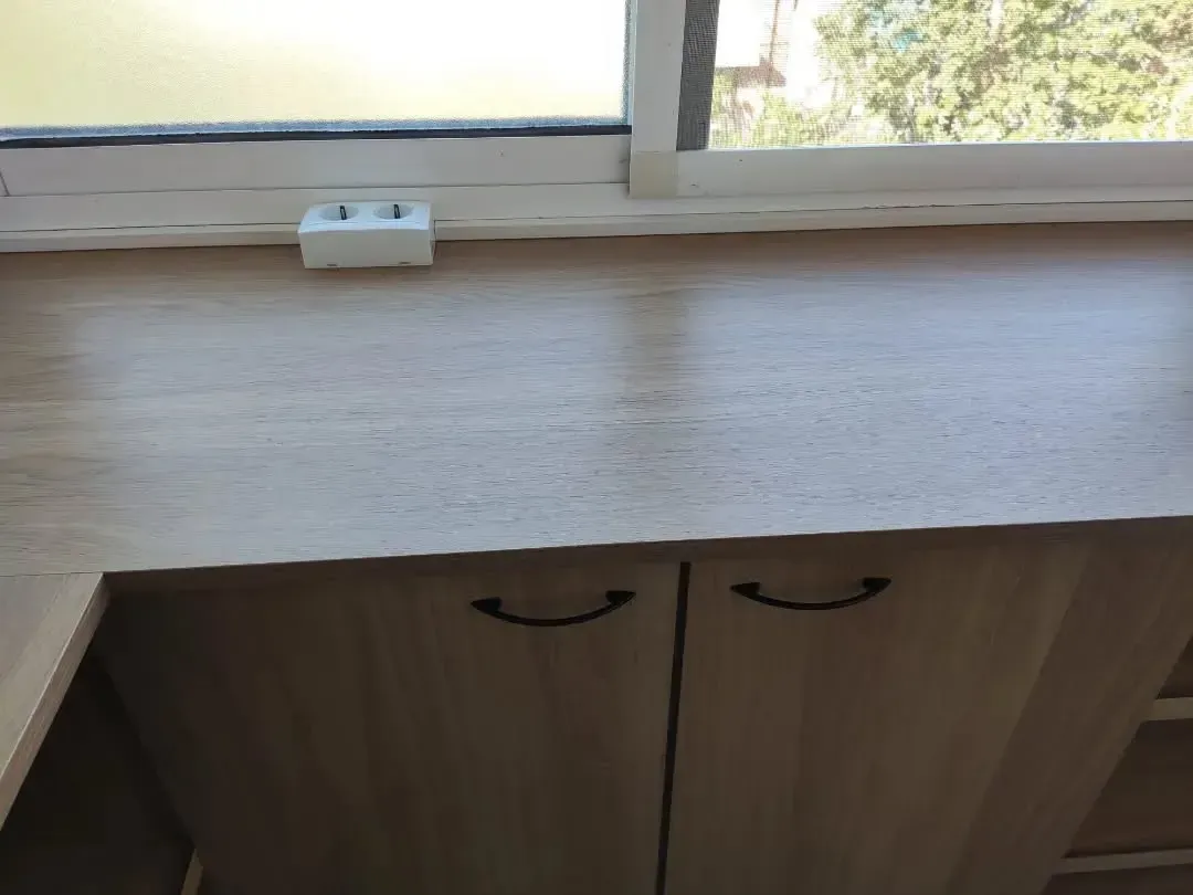 Un escritorio de madera con puertas de armario, una toma de corriente y una ventana al fondo.