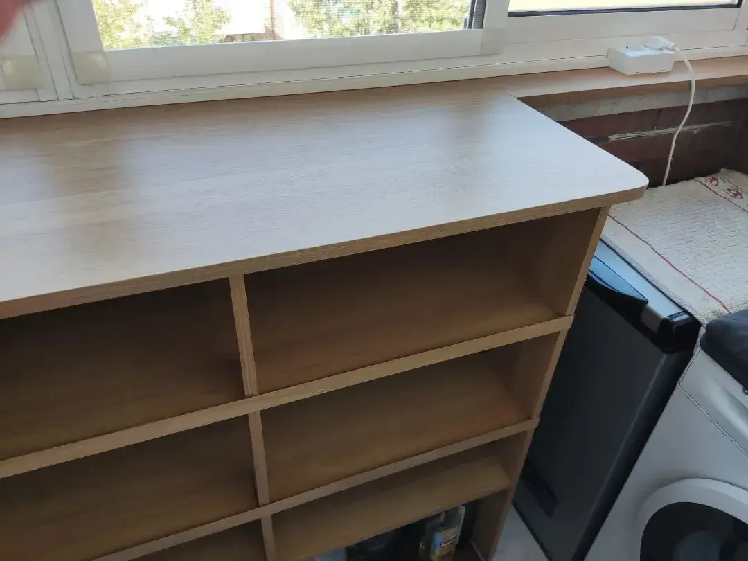 Mueble de madera clara con múltiples estantes abiertos, junto a una ventana.