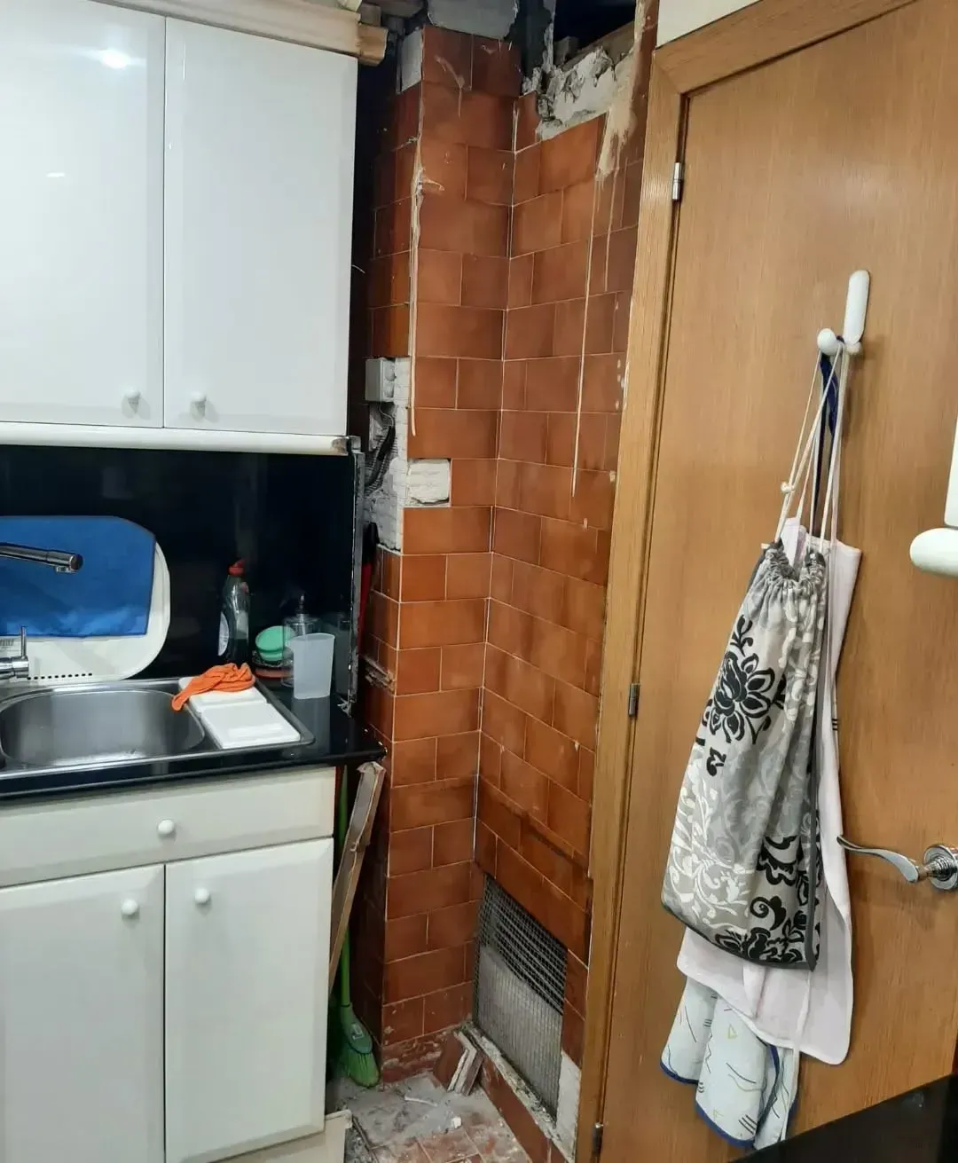 Cocina con gabinetes blancos, encimera oscura y pared de azulejos; puerta a la derecha con elementos colgados.