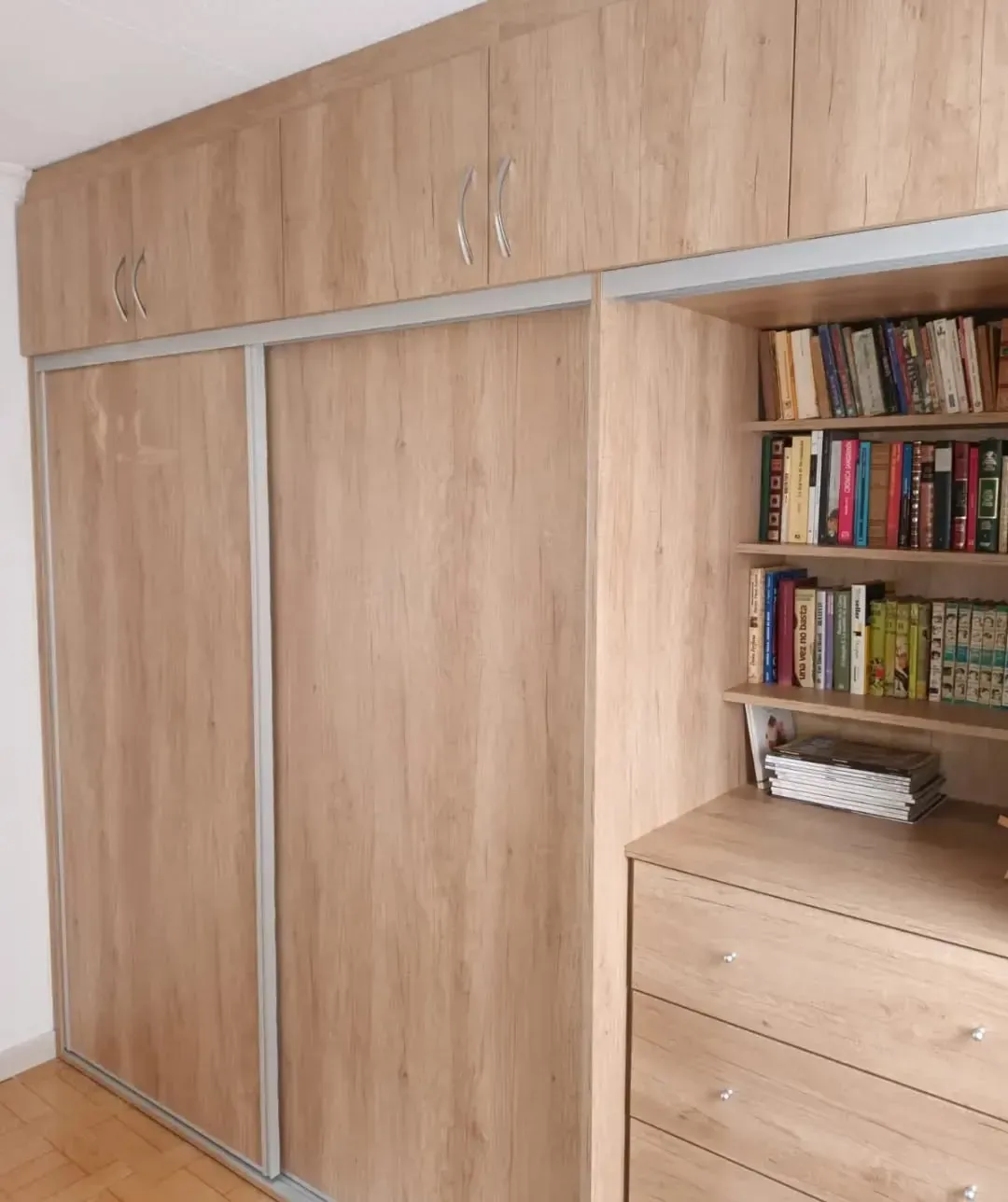 Armario de madera con puertas corredizas, muebles superiores y estantes abiertos con libros.