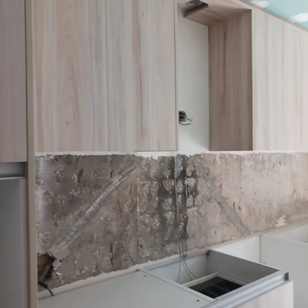 Gabinetes de cocina instalados sobre una pared rugosa, con paneles de yeso sin terminar y una base de fregadero debajo.