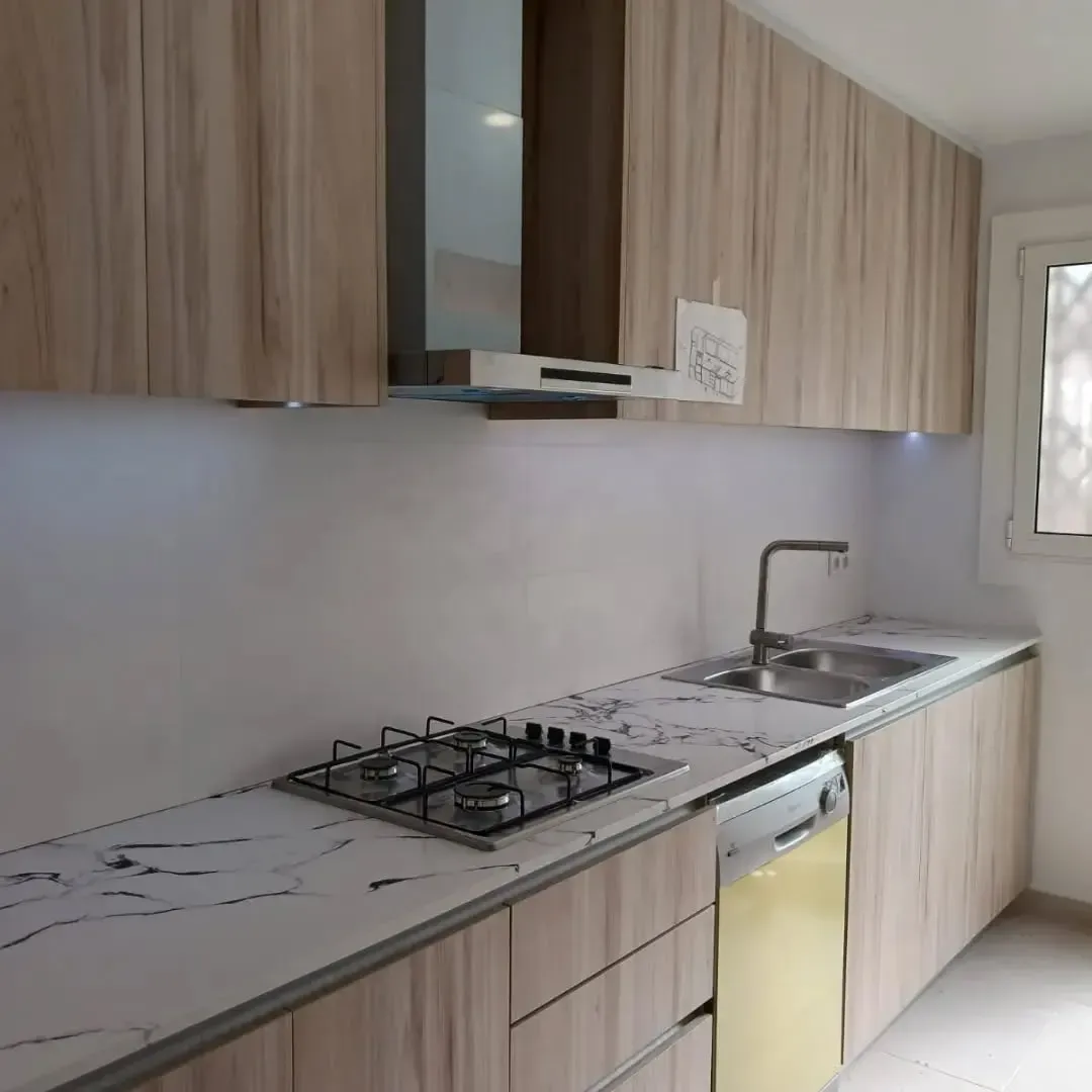 Cocina moderna con gabinetes de madera clara, encimeras blancas y electrodomésticos de acero inoxidable.