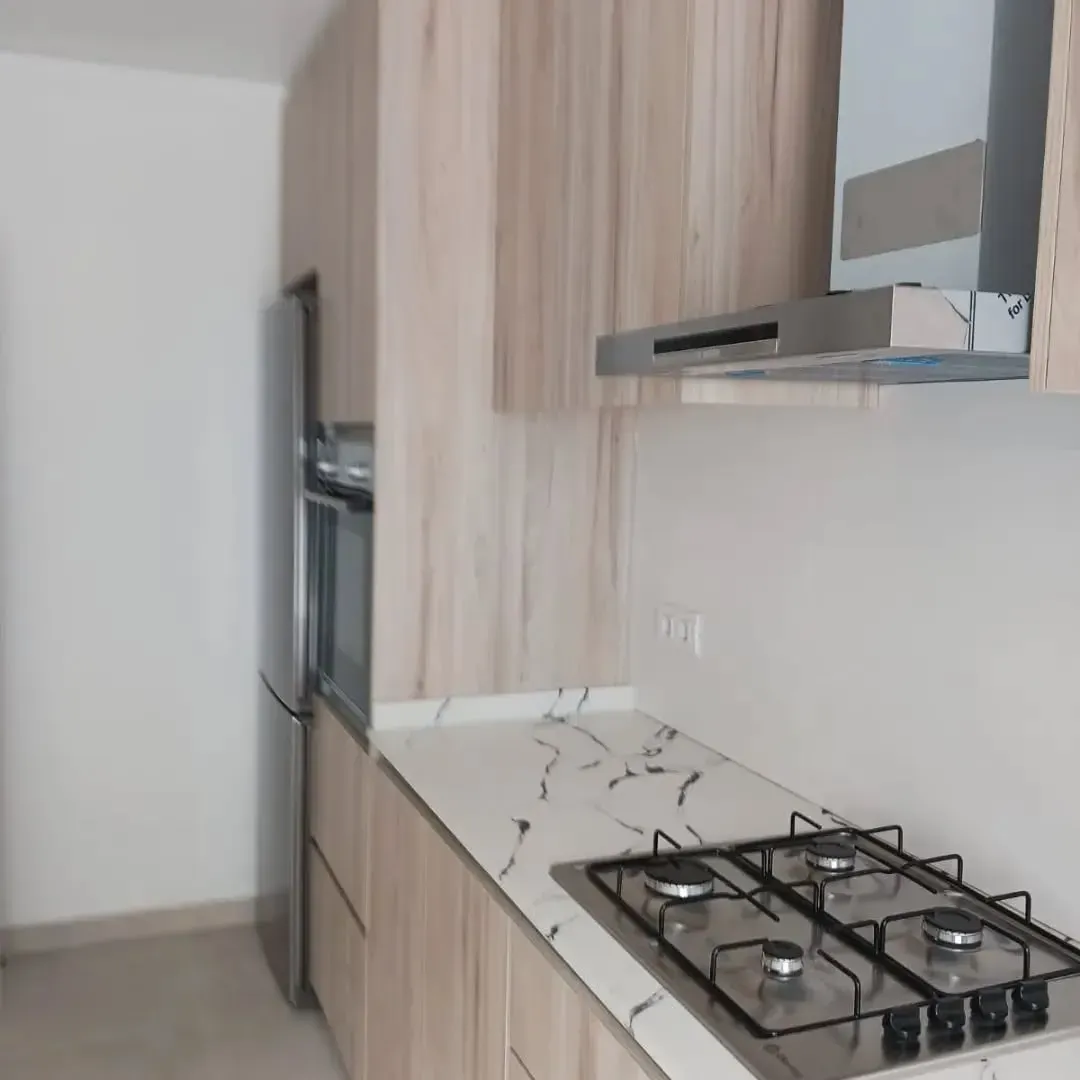 Cocina moderna con gabinetes de madera clara, encimeras blancas y electrodomésticos de acero inoxidable.