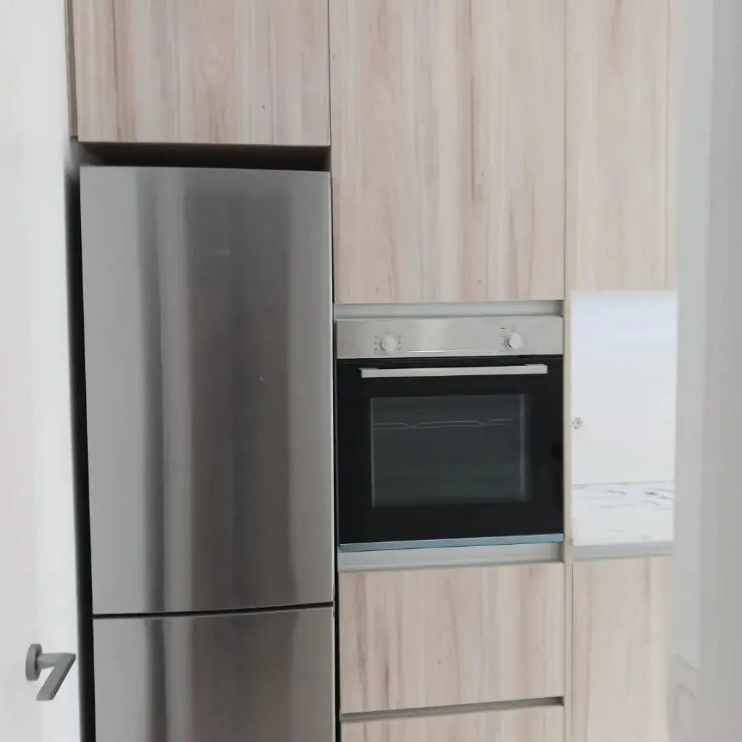 Muebles de cocina con refrigerador de acero inoxidable, horno y gabinetes en tono madera.