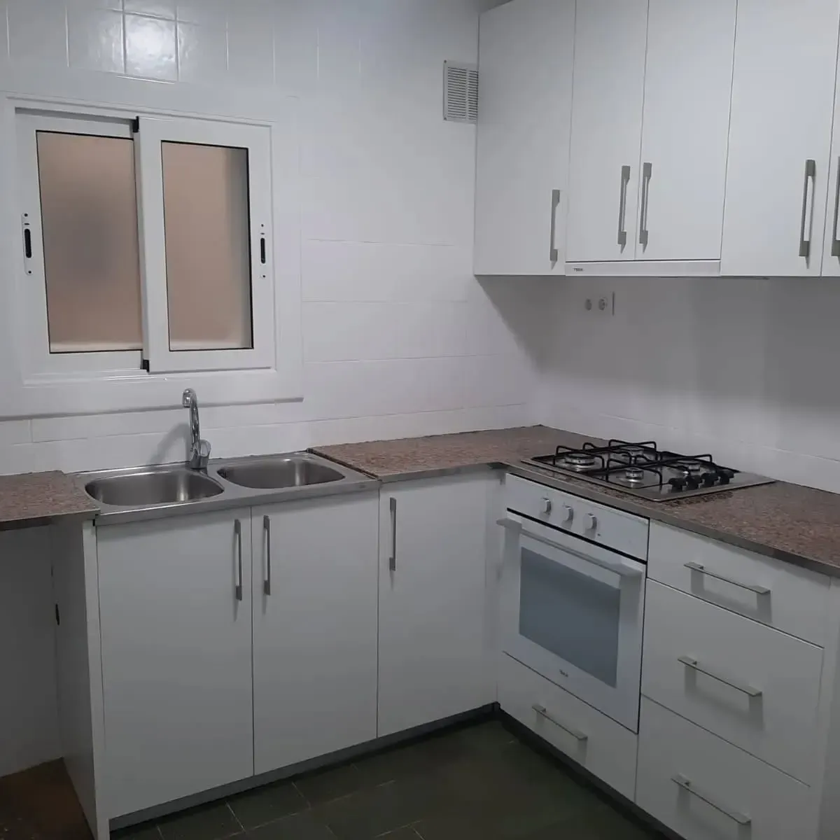 Cocina blanca con fregadero, estufa y gabinetes de acero inoxidable. Encimeras marrones y ventana esmerilada.