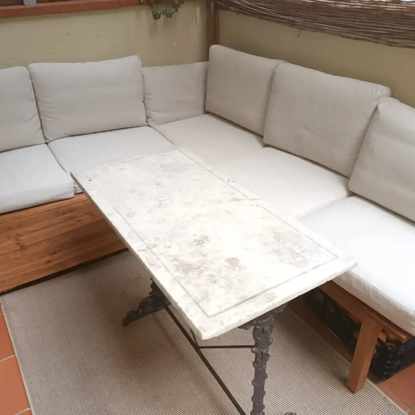 Zona de estar en el patio al aire libre con una mesa con cubierta de mármol blanco y cojines de color crema.