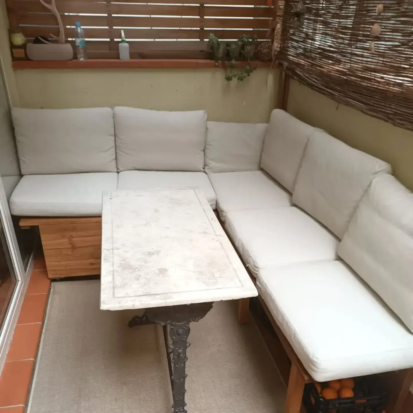 Patio al aire libre con asientos acolchados blancos, muebles de madera y una mesa.