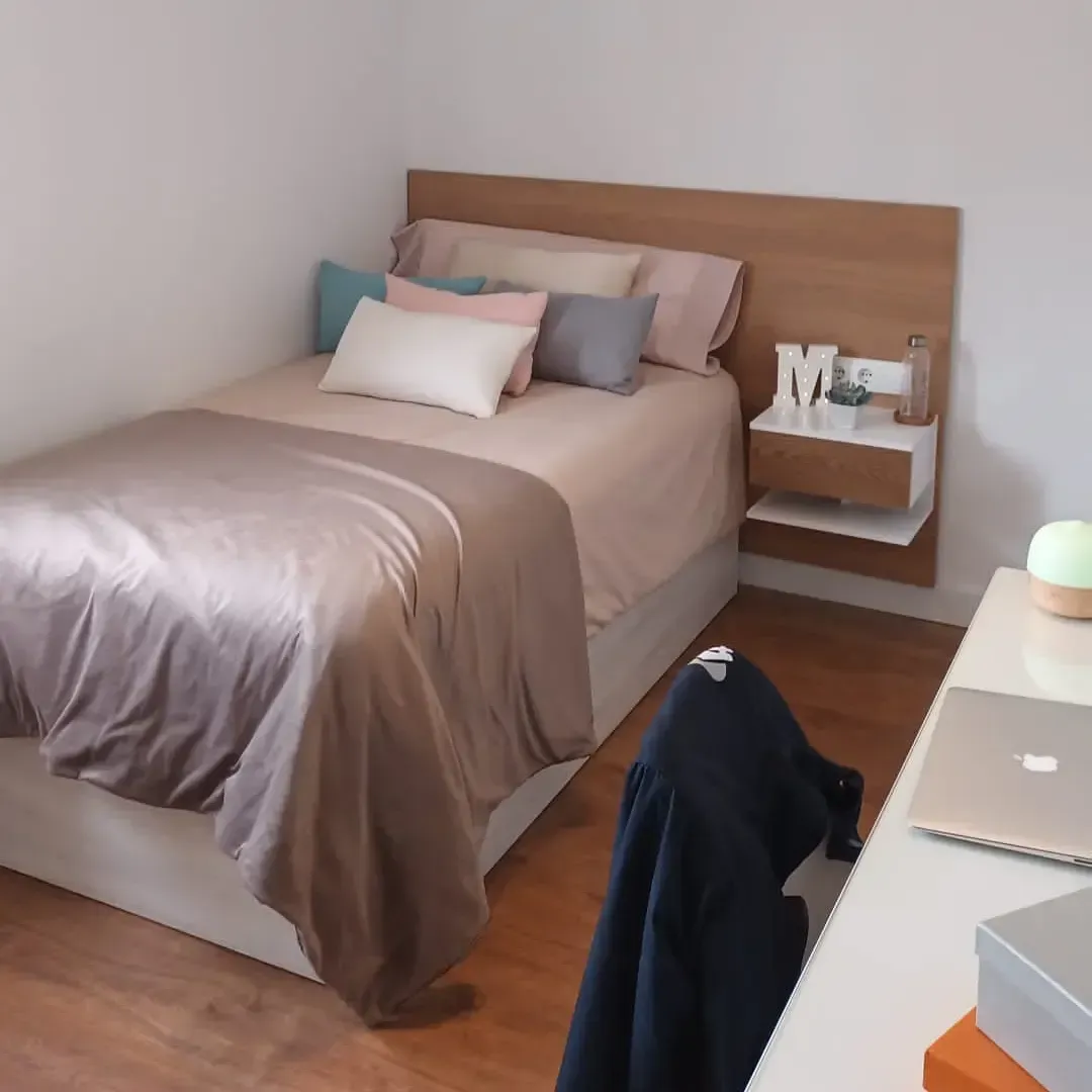 Dormitorio con cama, escritorio, mesita de noche flotante y varias almohadas.