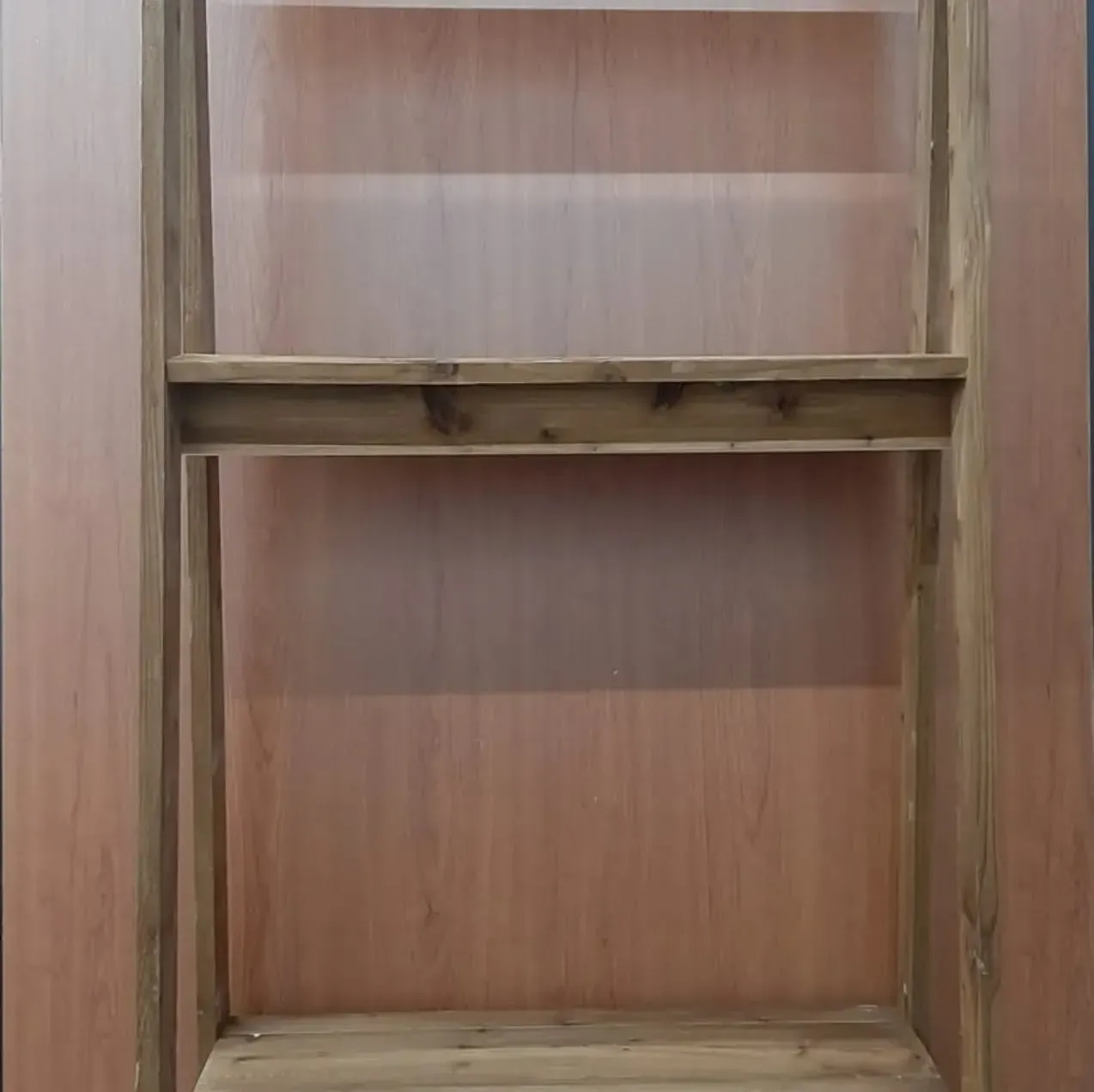 Estantería de madera con dos estantes contra una pared de color marrón claro.