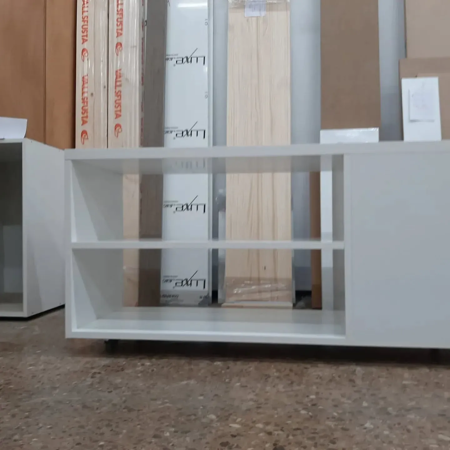 Consola multimedia blanca con estantes abiertos y un armario, en un entorno de almacén.