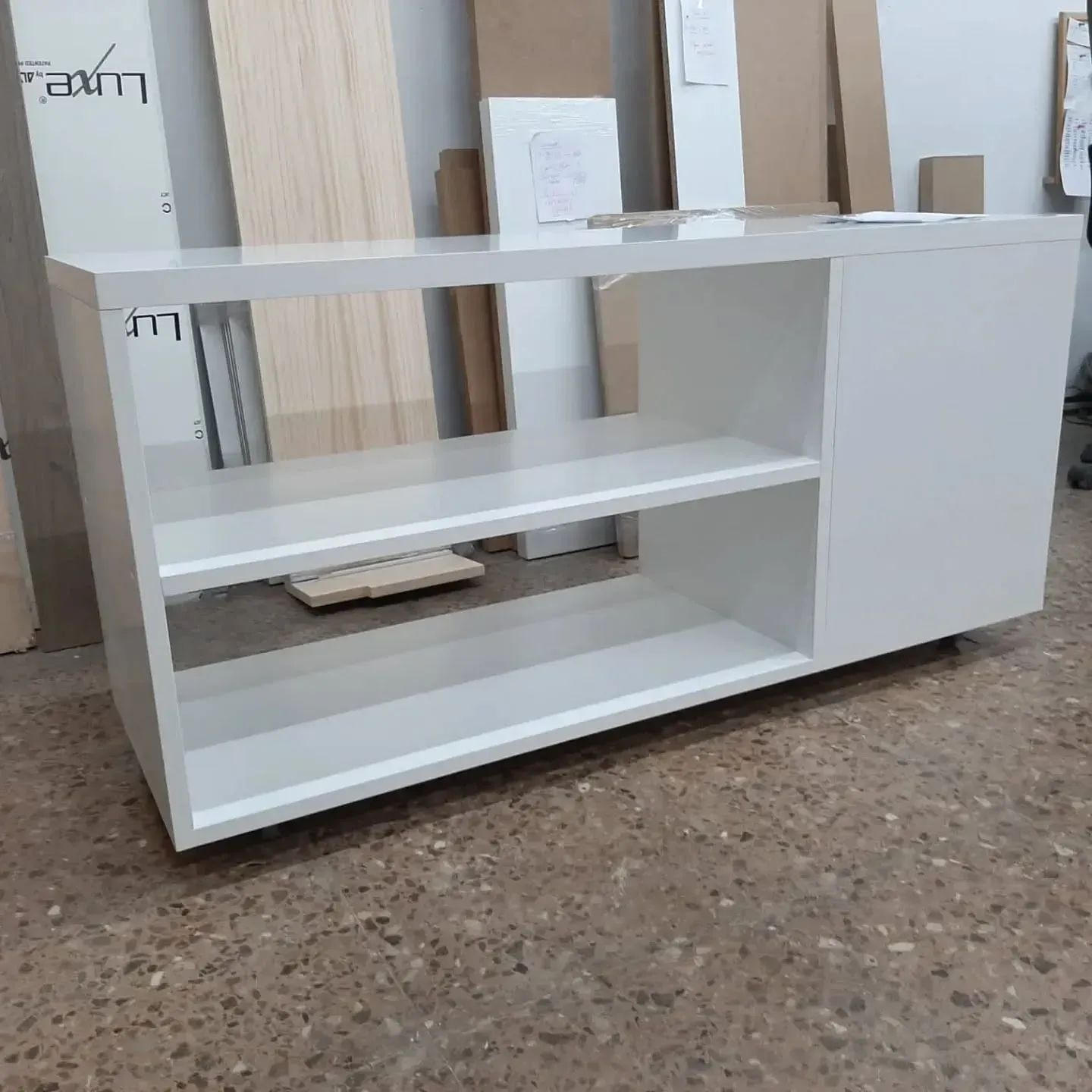 Centro de entretenimiento moderno de color blanco con estantes abiertos y un mueble sobre suelo de hormigón.