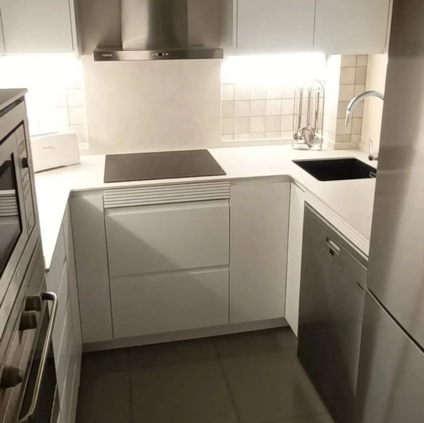 Cocina moderna, blanca con electrodomésticos integrados y detalles de acero inoxidable.