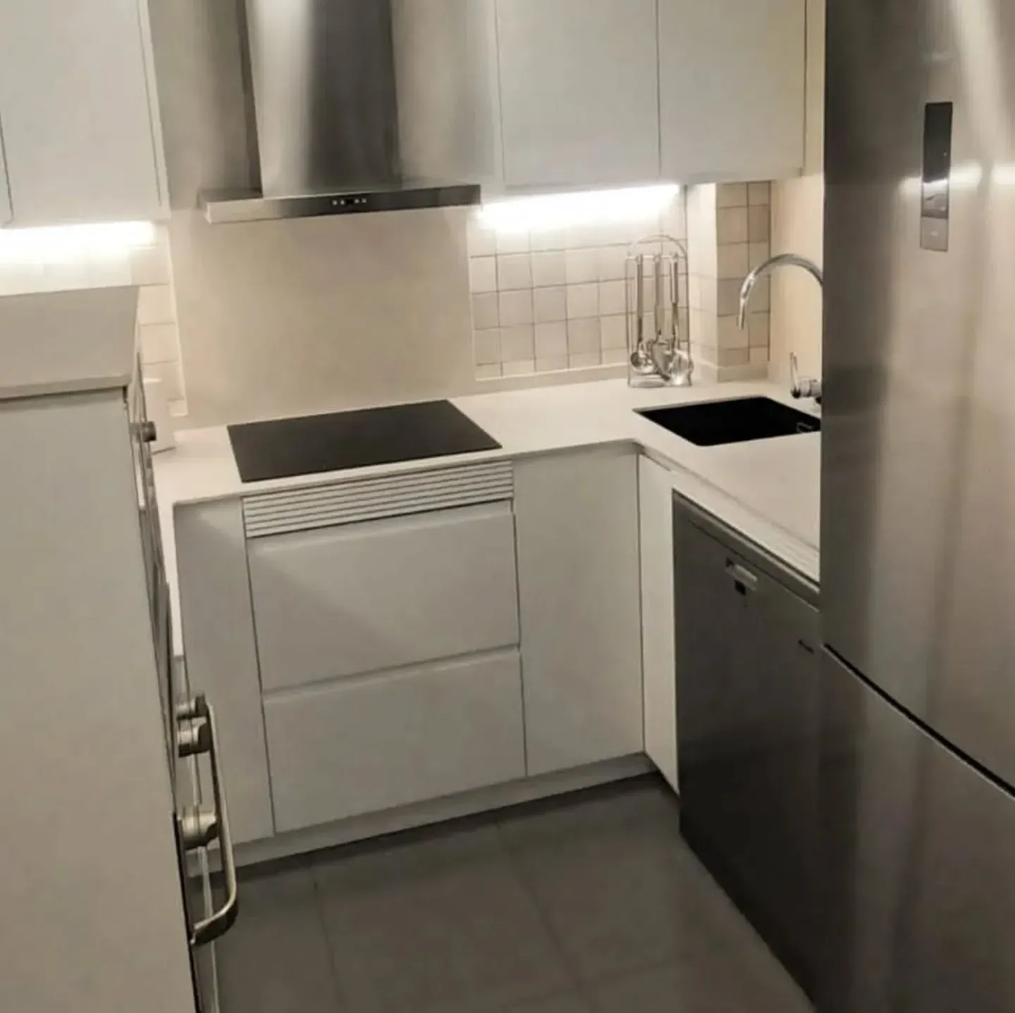 Cocina blanca en forma de L con electrodomésticos de acero inoxidable, estufa oscura 