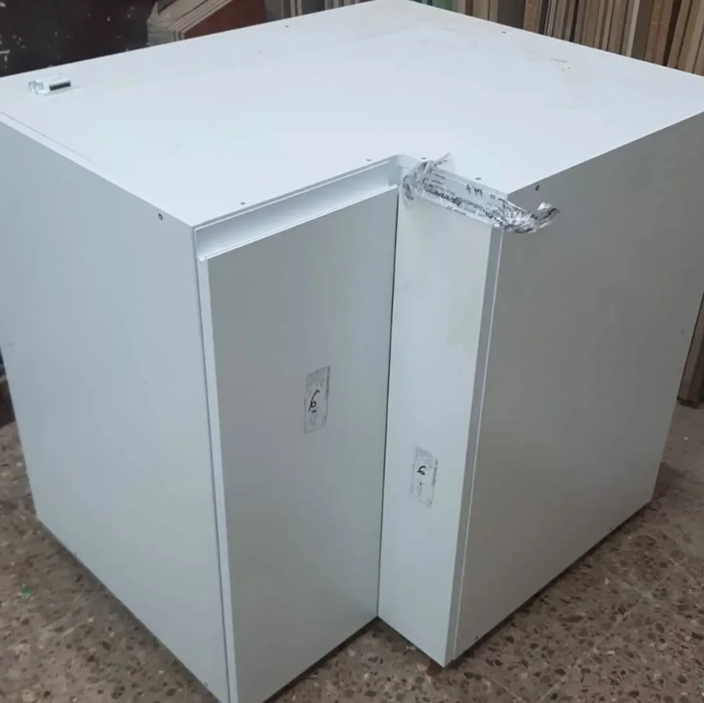 Armario blanco en forma de L, posiblemente para cocina. Tiene dos puertas y herrajes visibles en un lateral.