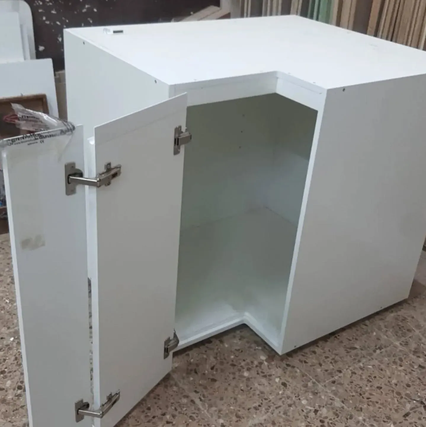 Armario blanco en forma de L con puerta abierta que deja ver el interior. Bisagras plateadas visibles.