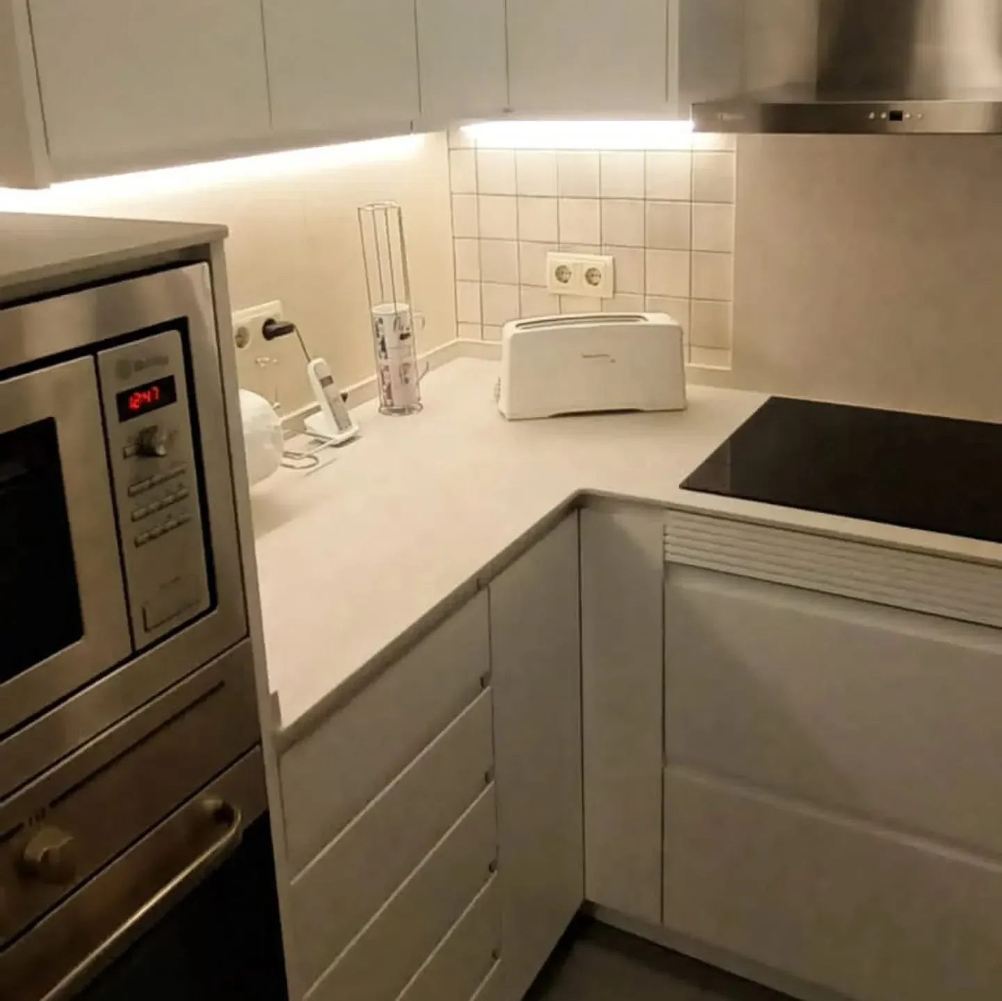 Cocina blanca con microondas, gabinetes y tostadora.