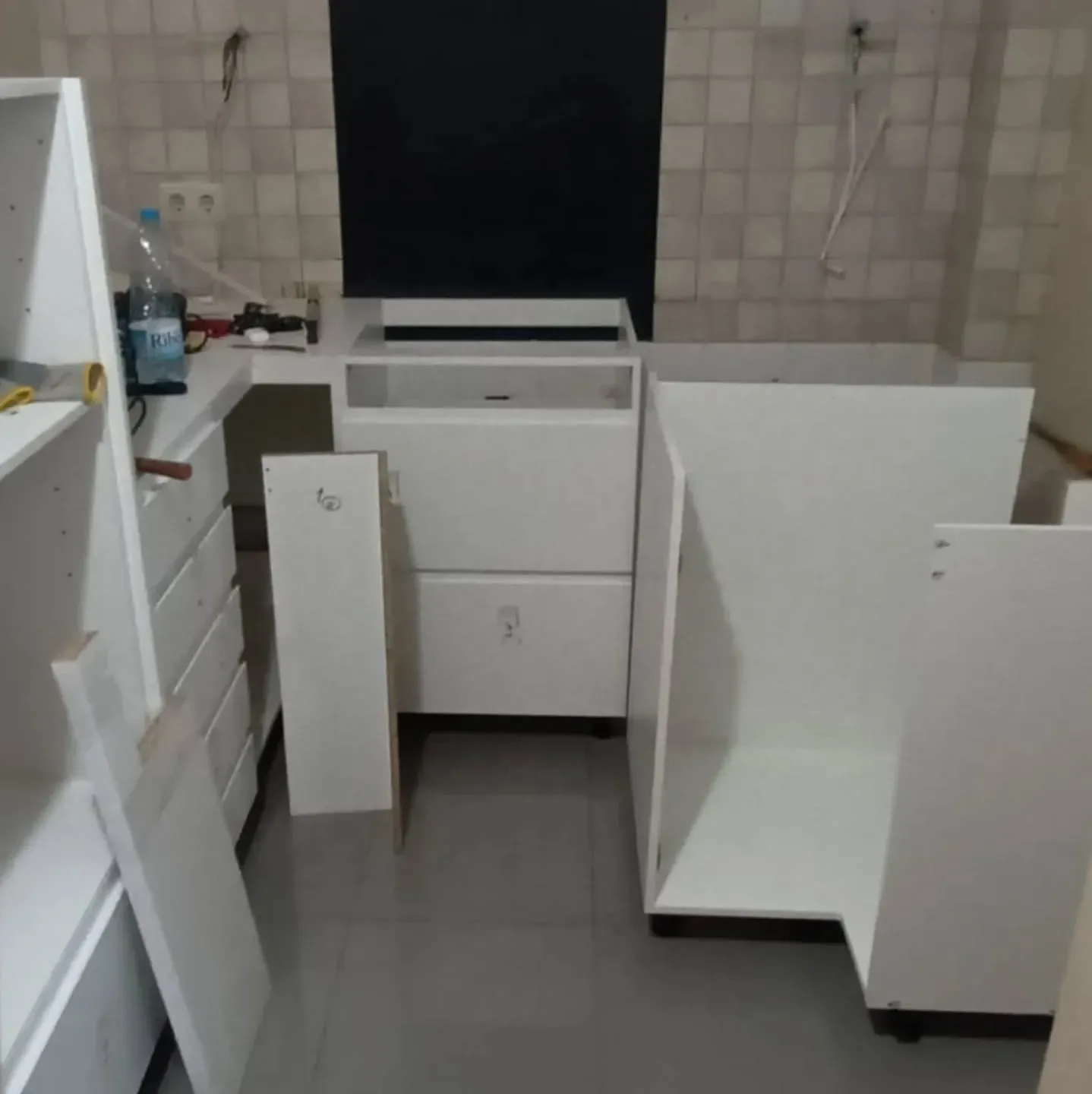 Gabinetes de cocina, en su mayoría blancos, en diversas etapas de ensamblaje. El entorno es una cocina.