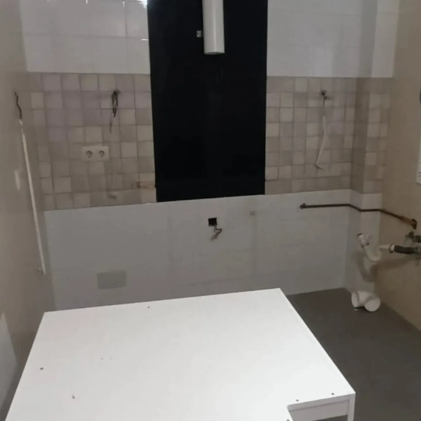 Cocina con gabinetes blancos, salpicadero de azulejos gris claro y un panel de color oscuro.