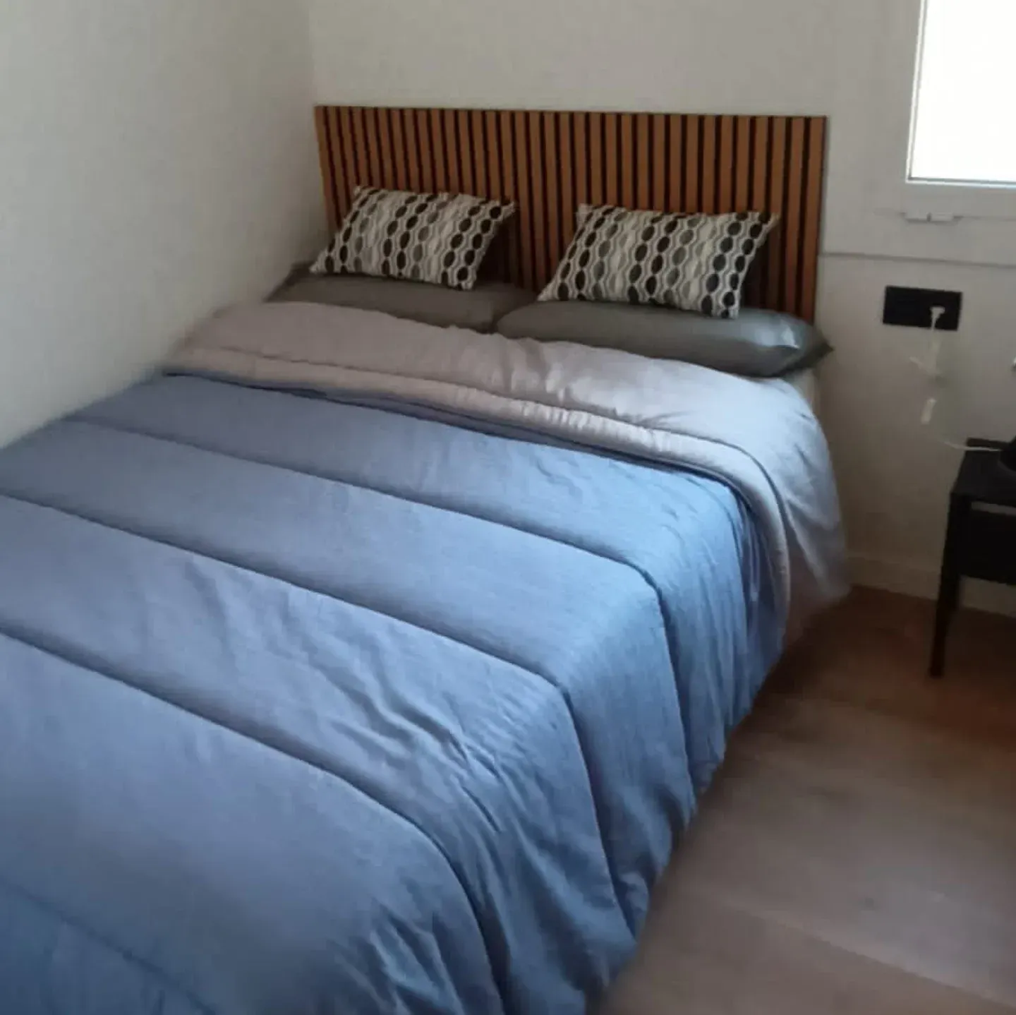 Una cama con ropa de cama azul, dos almohadas y un cabecero de madera en un dormitorio.