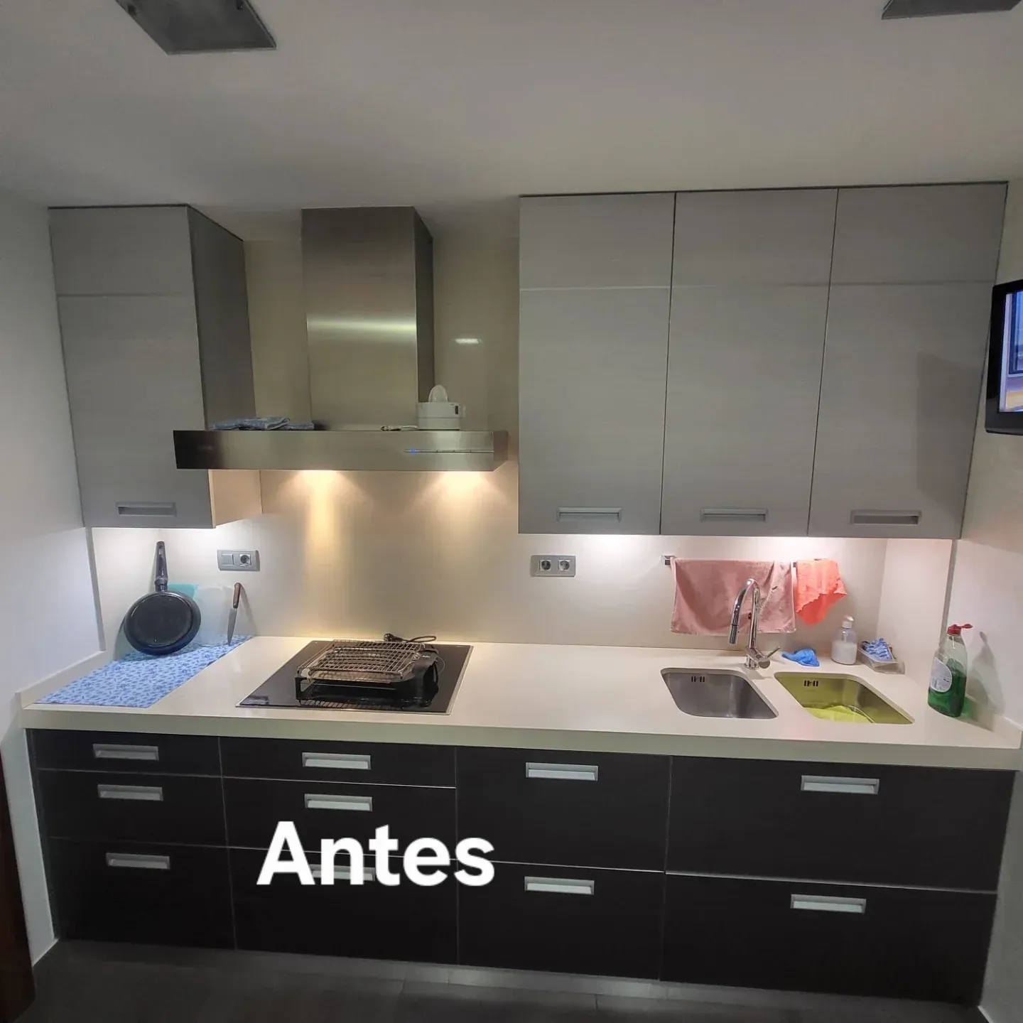 Cocina con gabinetes grises y negros, encimera, estufa, campana extractora y fregadero. Texto 