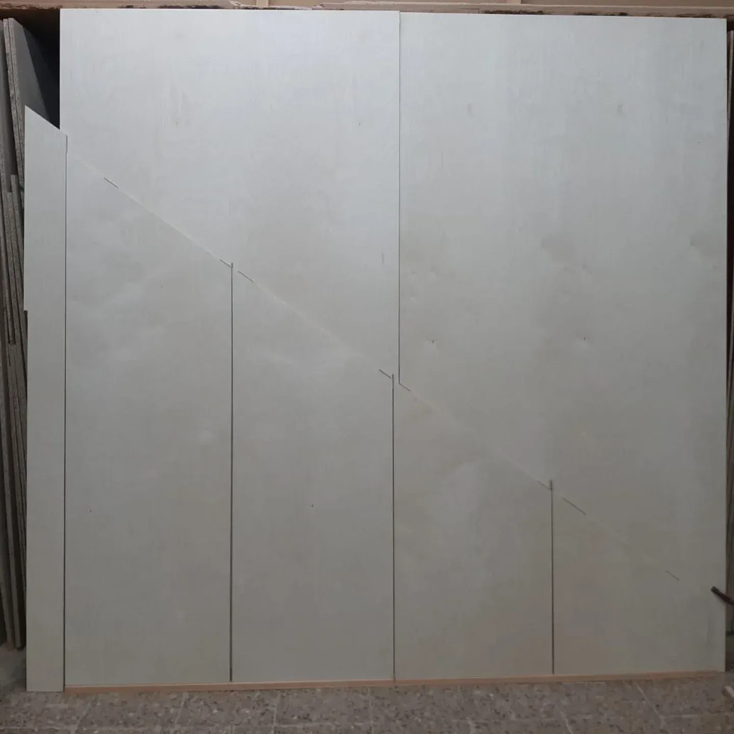 Grandes paneles de madera de color claro dispuestos sobre un suelo, con uno de los paneles cortado en diagonal.