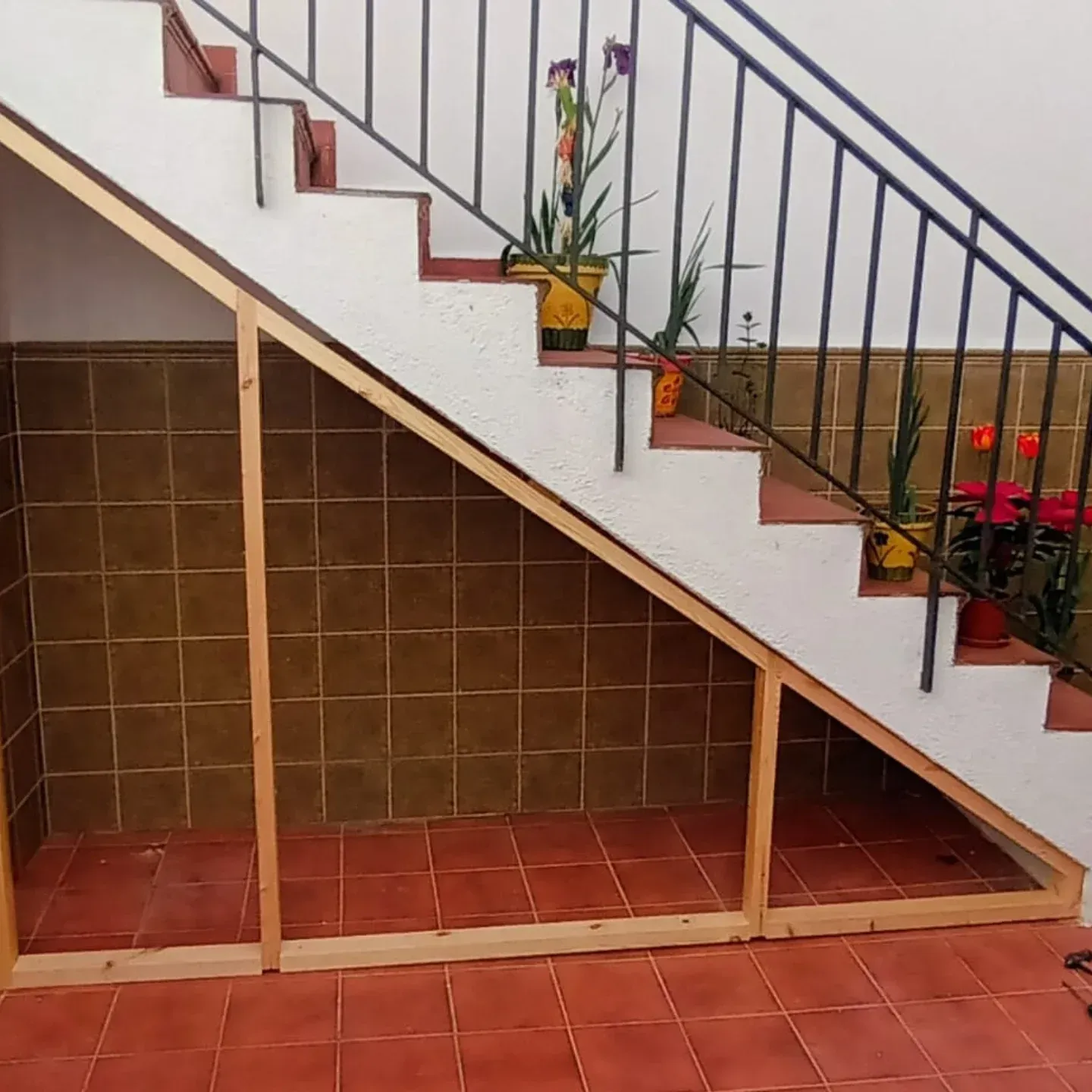 Marco de madera debajo de las escaleras, contra una pared de azulejos marrones y un piso de azulejos rojos.