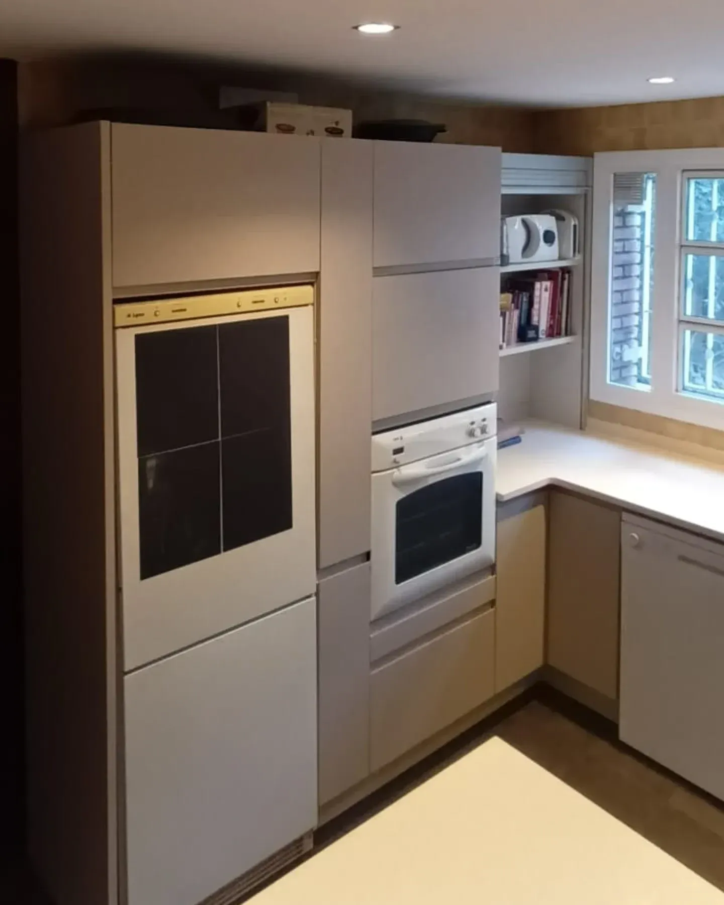 Cocina con gabinetes color gris claro, electrodomésticos blancos y una ventana.