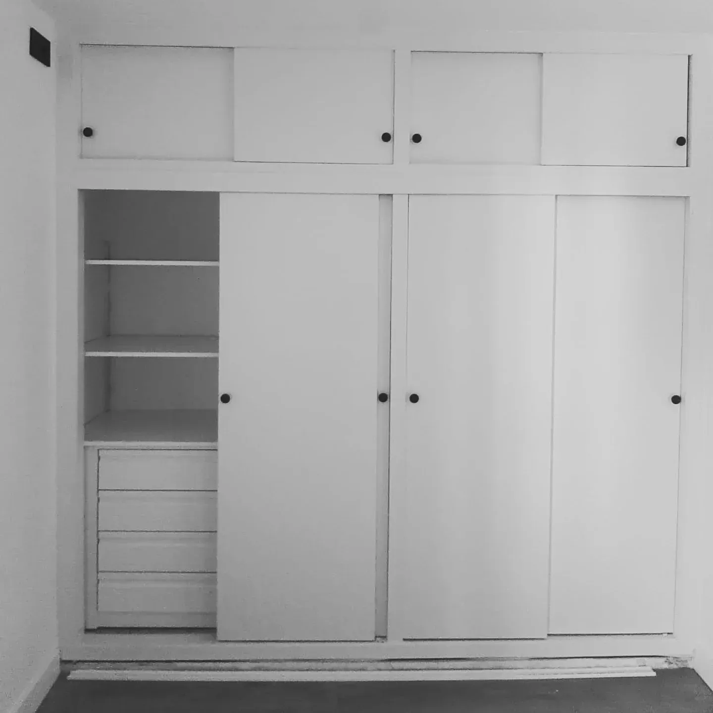 Armario empotrado blanco con puertas correderas y espacio de almacenamiento superior. Incluye estantes y cajones.