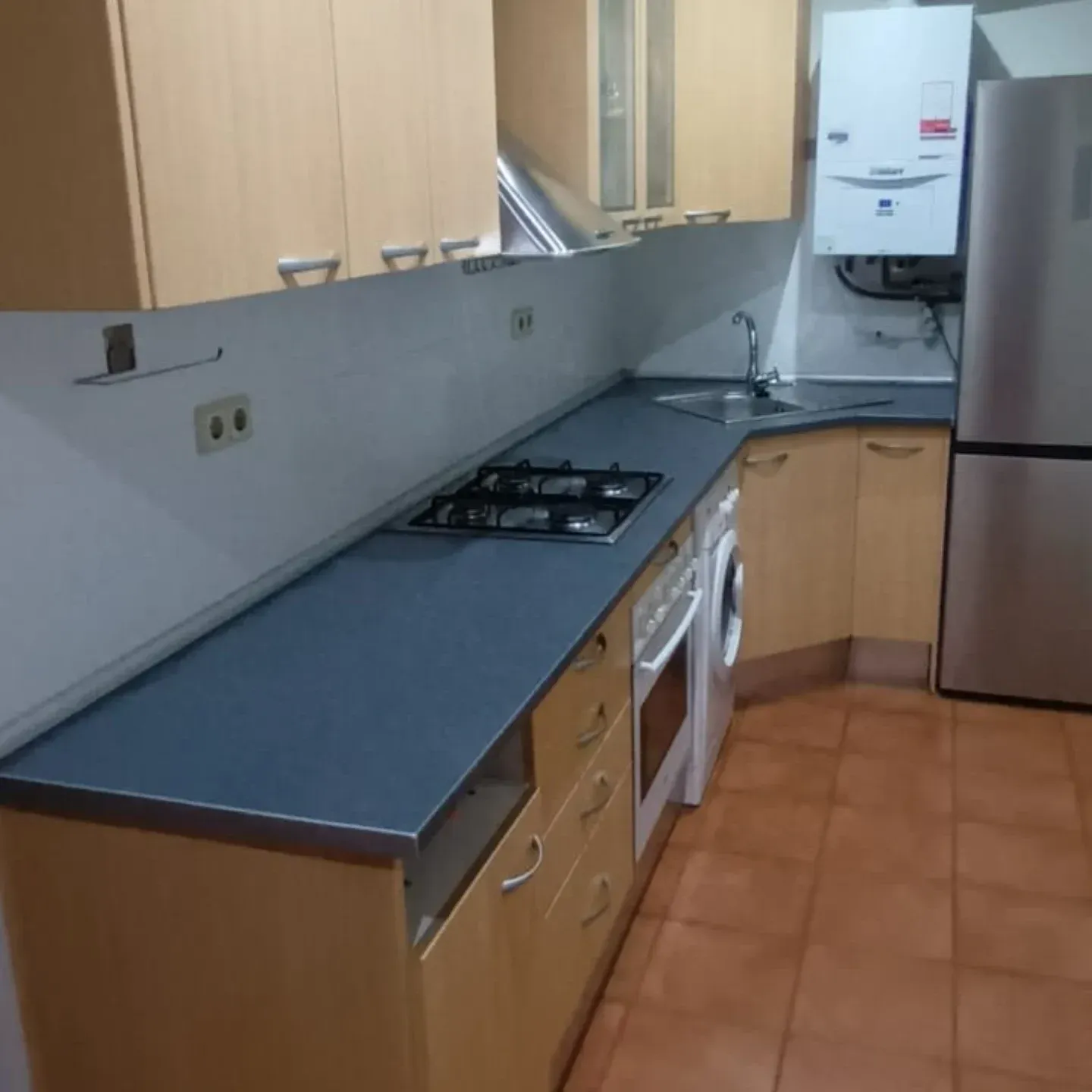 Cocina con gabinetes de madera clara, encimeras grises y electrodomésticos de acero inoxidable.