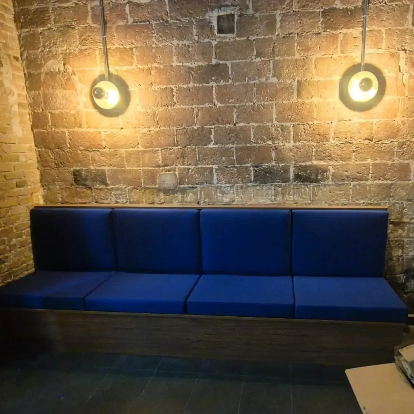 Banco azul contra una pared de ladrillos, iluminado por dos lámparas colgantes.
